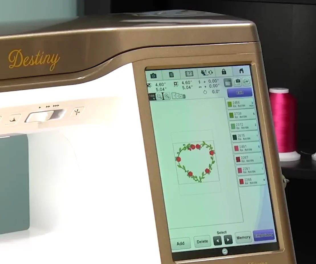 Embroidery machine screen displaying a floral heart design, hoop size, and thread color sequence.